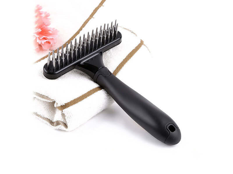 Pet hair removal brush with ergonomic handle on towel, featuring stainless steel bristles for effective pet hair cleaning.